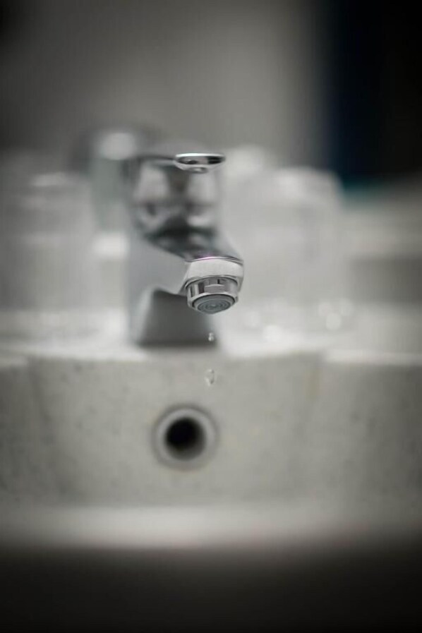 Gros plan d’un robinet d’où coule de l’eau, faisant partie d’un lavabo de salle de bain.