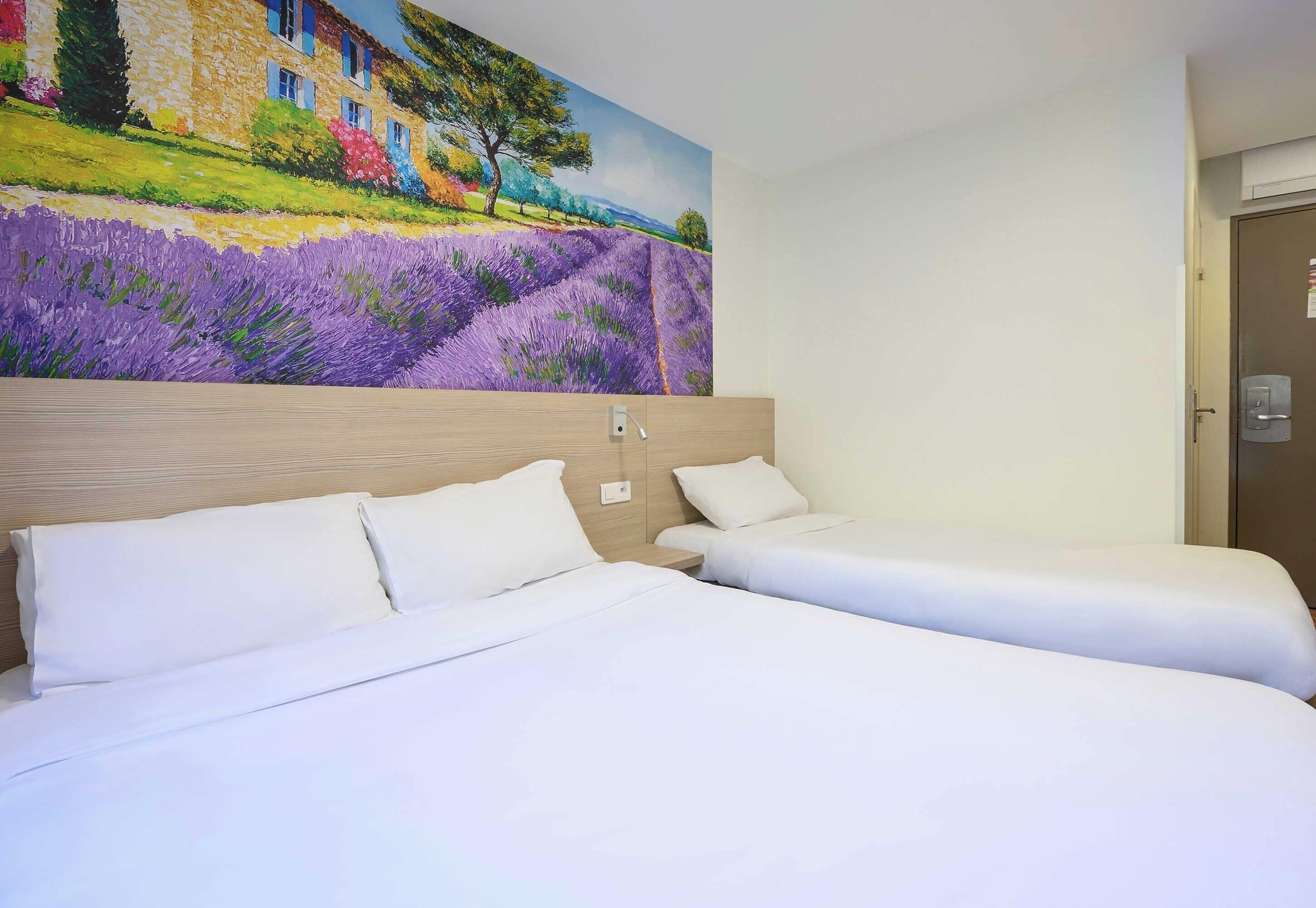 Une chambre d’hôtel avec deux lits, une tête de lit en bois et un grand tableau représentant un paysage.