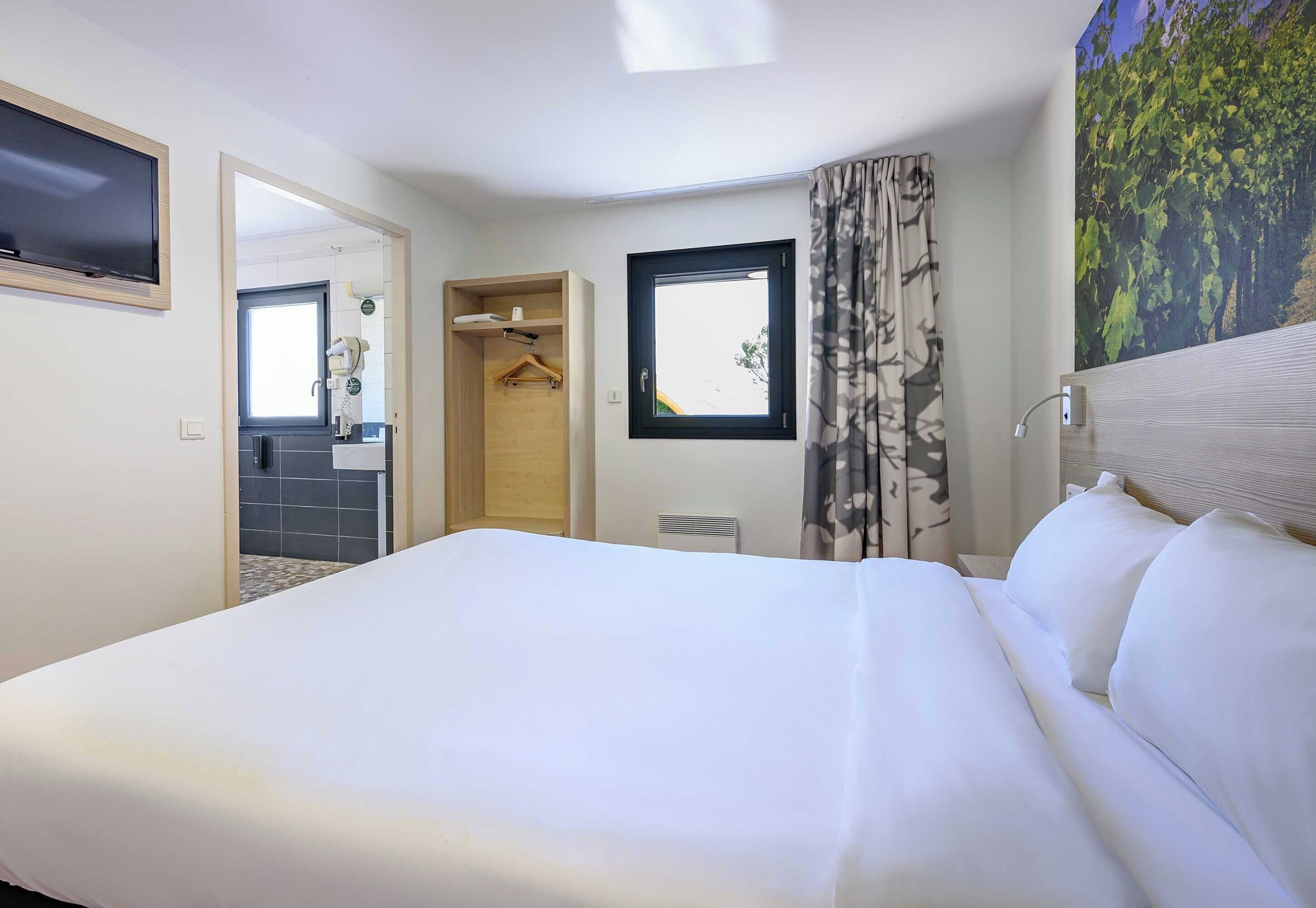 Une chambre d’hôtel avec un grand lit, une salle de bain avec un miroir et une fenêtre avec des rideaux.