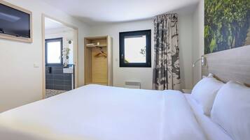 Une chambre d’hôtel avec un grand lit, une salle de bain avec un miroir et une fenêtre avec des rideaux.