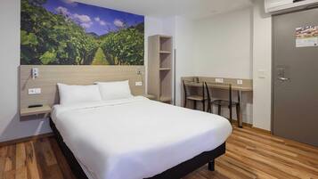 A hotel room with a bed, a desk, a chair, a wardrobe, and a wall-mounted air conditioner.