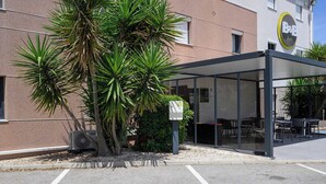 Un hotel con una zona de estar al aire libre cubierta, un edificio con un letrero y un estacionamiento.
