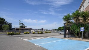 A parking area with a blue handicapped parking space, a bus stop, and a building with a sign that reads 'Boulanger Pâtisserie'. - B&B HOTEL BOLLENE (Bollene)
