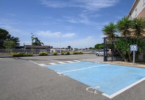 Un área de estacionamiento con un espacio reservado para discapacitados de color azul, una parada de autobús y un edificio con un letrero que dice 'Boulanger Pâtisserie'.