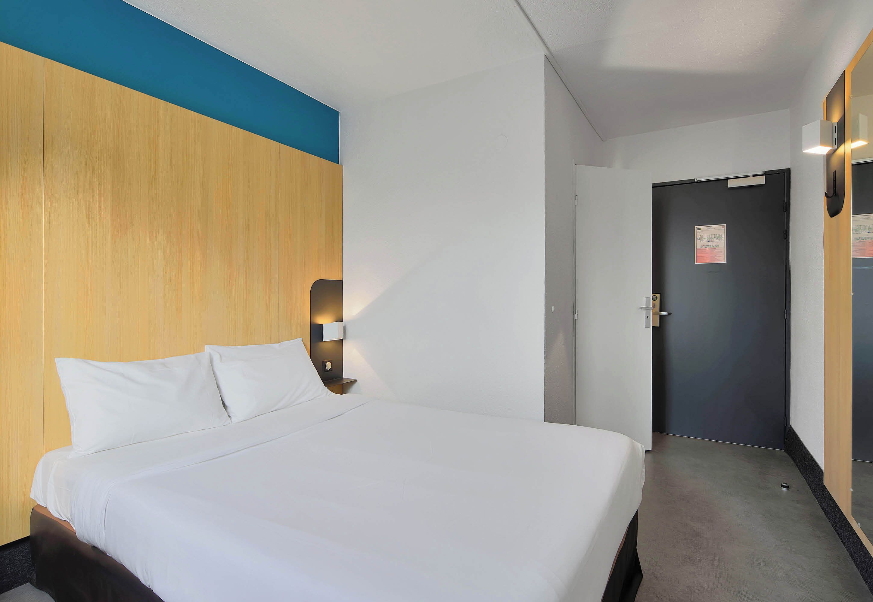 Et hotelværelse med en stor seng, et træhovedgærde, et natbord med en lampe og en dør med et skilt.