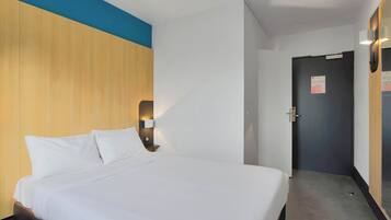 Et hotelværelse med en stor seng, et træhovedgærde, et natbord med en lampe og en dør med et skilt.