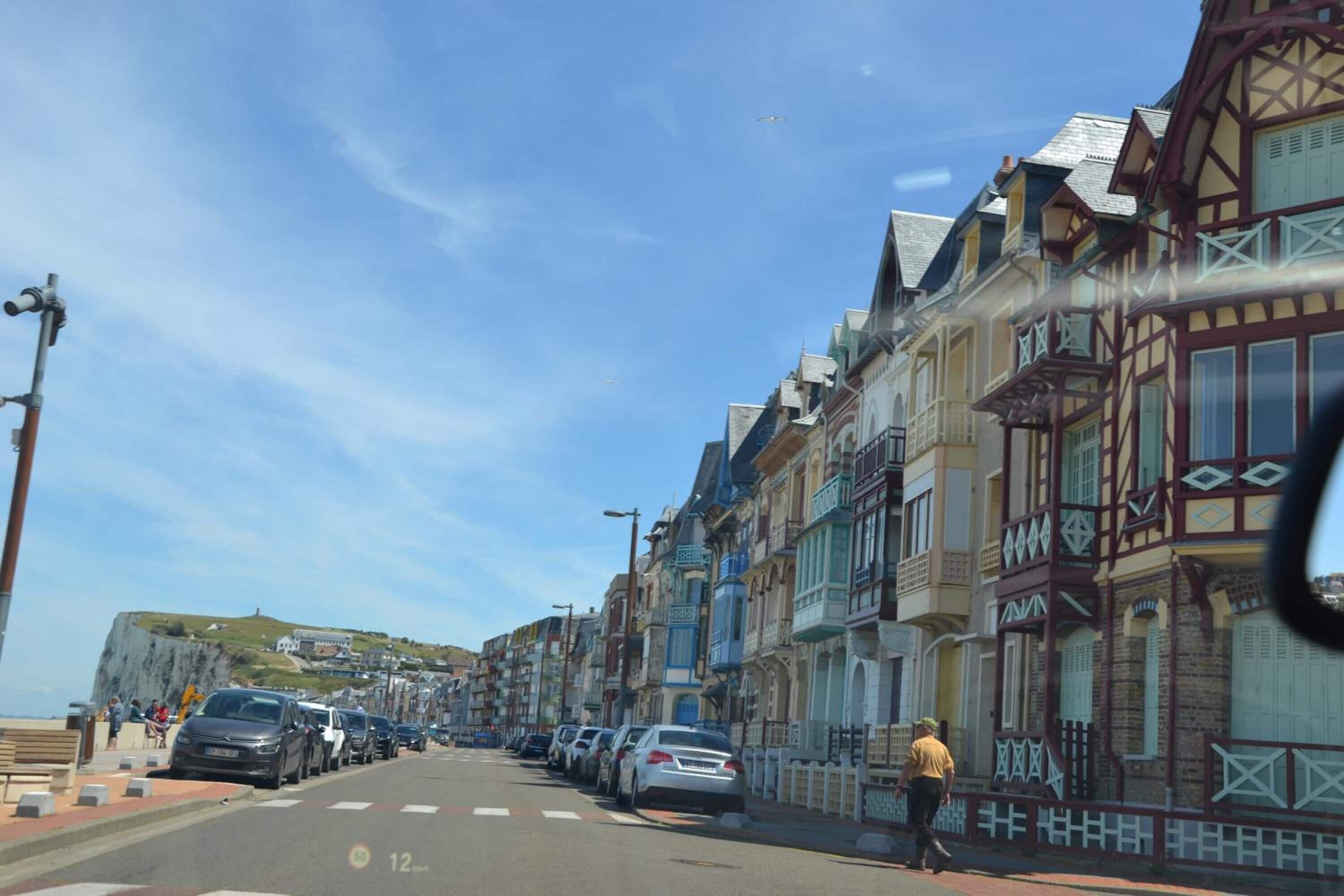 A street lined with colorful buildings, parked cars, and a pedestrian.