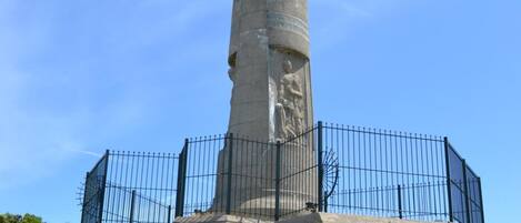 Un monumento alto con una estatua en la cima, rodeado por una valla metálica.