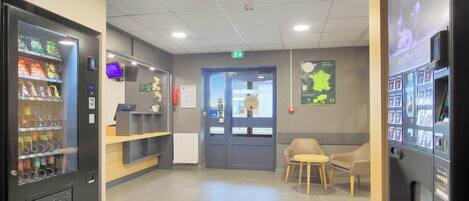 Eine moderne Lobby mit Getränkeautomaten, einer Rezeption und einer Sitzecke.