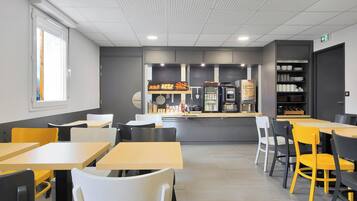 Un espace repas moderne avec des tables et des chaises, un comptoir où sont présentés des aliments et un réfrigérateur.