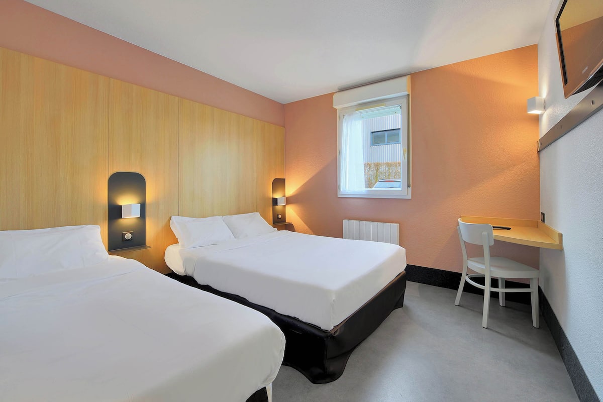 A hotel room with two beds, a desk, and a chair.