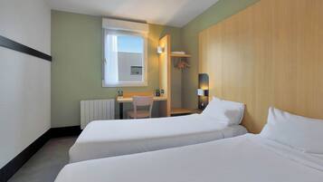 A hotel room with two beds, a desk, a chair, a radiator, and a window.
