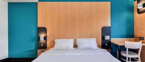 A modern hotel room with a large bed, a desk, and a chair.