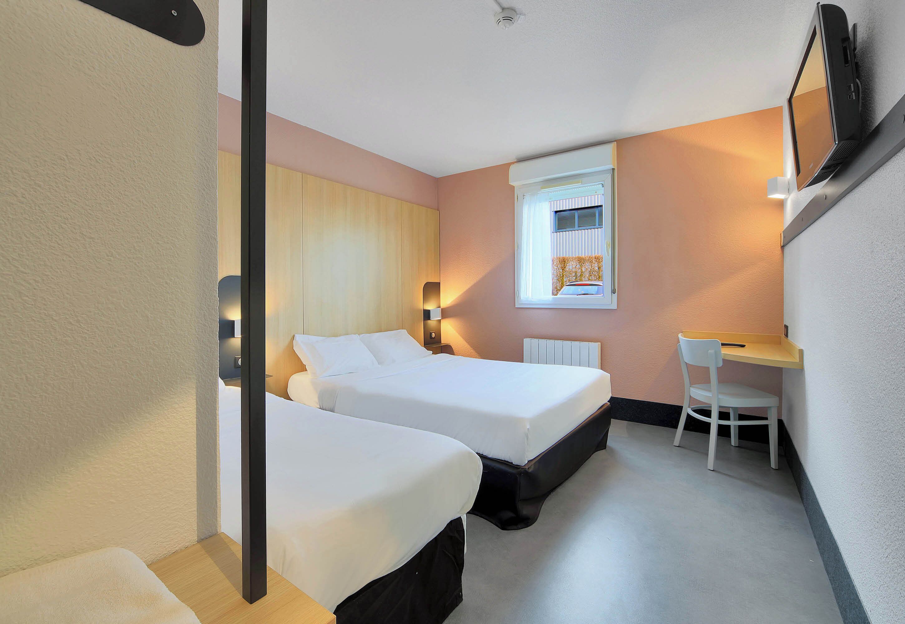 Habitación de hotel con dos camas, un escritorio y una silla.