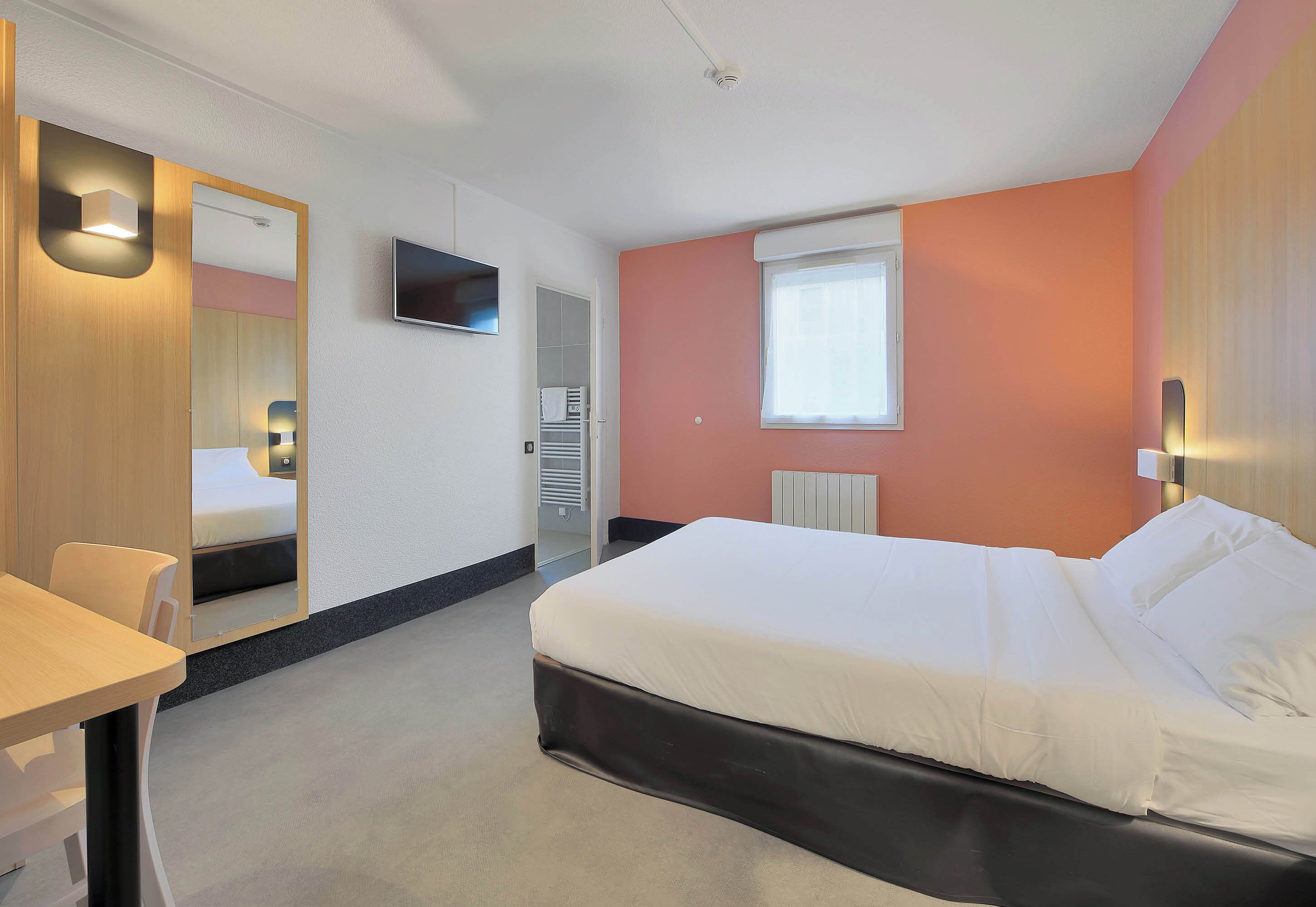 Una habitación de hotel con cama, escritorio, silla, televisor y ventana.