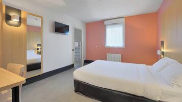 A hotel room with a bed, a desk, a chair, a TV, and a window.