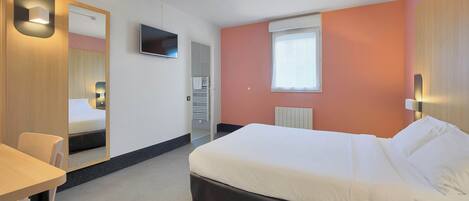 Una habitación de hotel con cama, escritorio, silla, televisor y ventana.