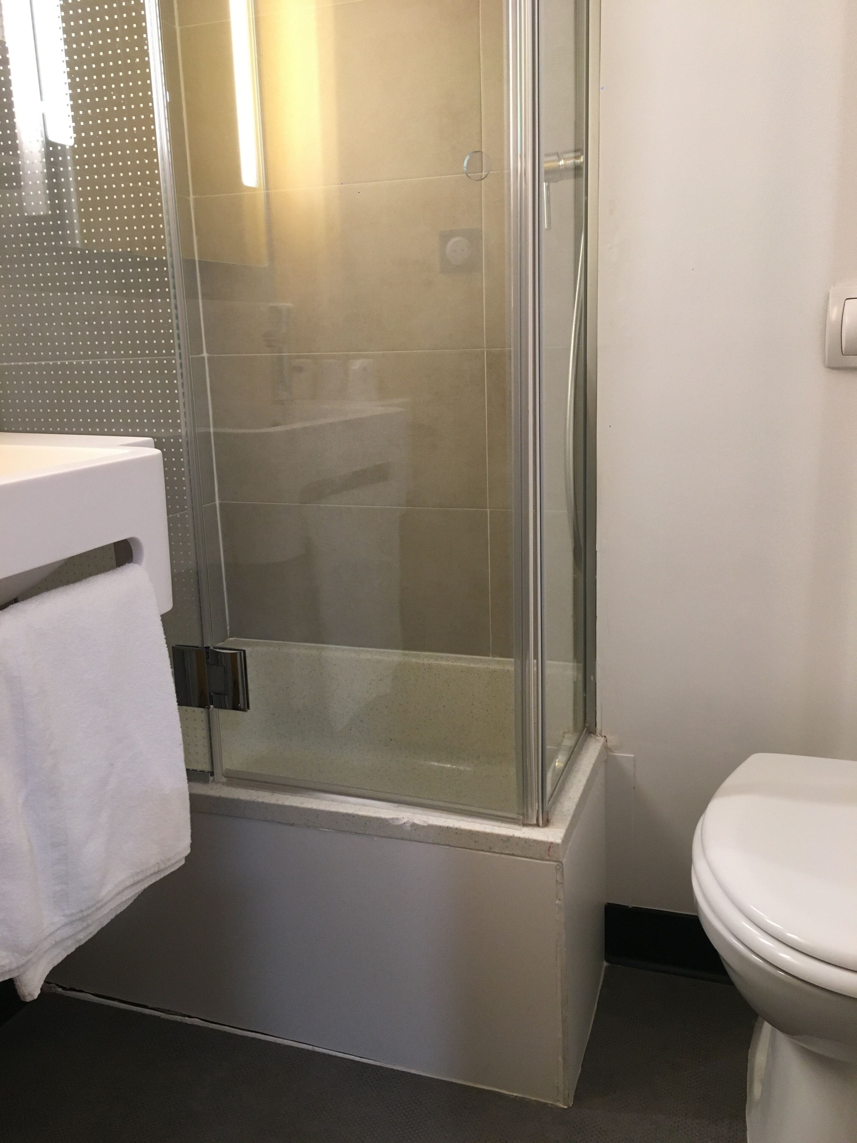 Une salle de bain moderne avec une douche à l’italienne en verre, des toilettes blanches et un lavabo blanc avec une serviette.