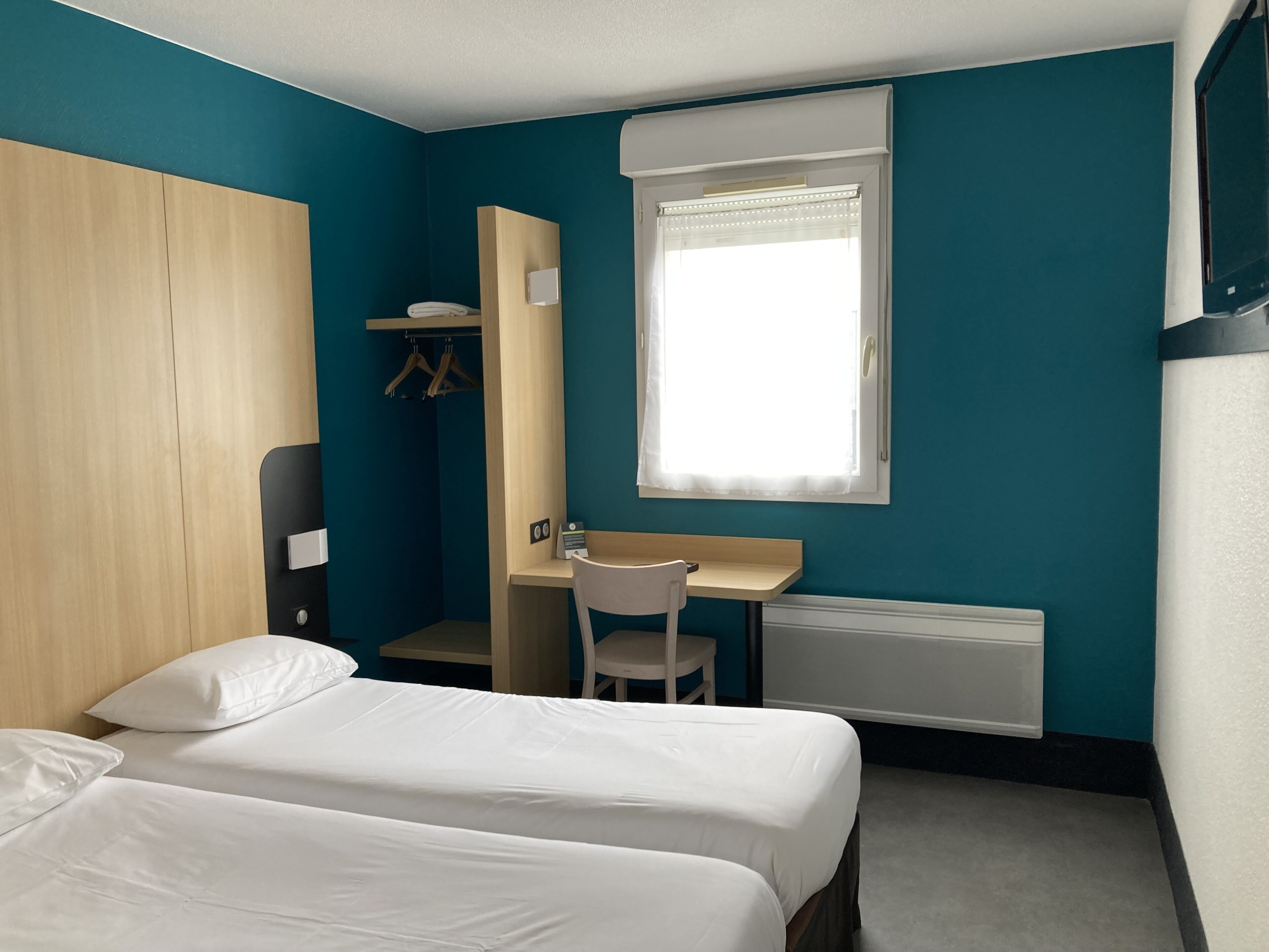 Ein Schlafzimmer mit zwei Betten, einem Schreibtisch, einem Stuhl, einem Kleiderschrank und einem Fenster mit Jalousien.