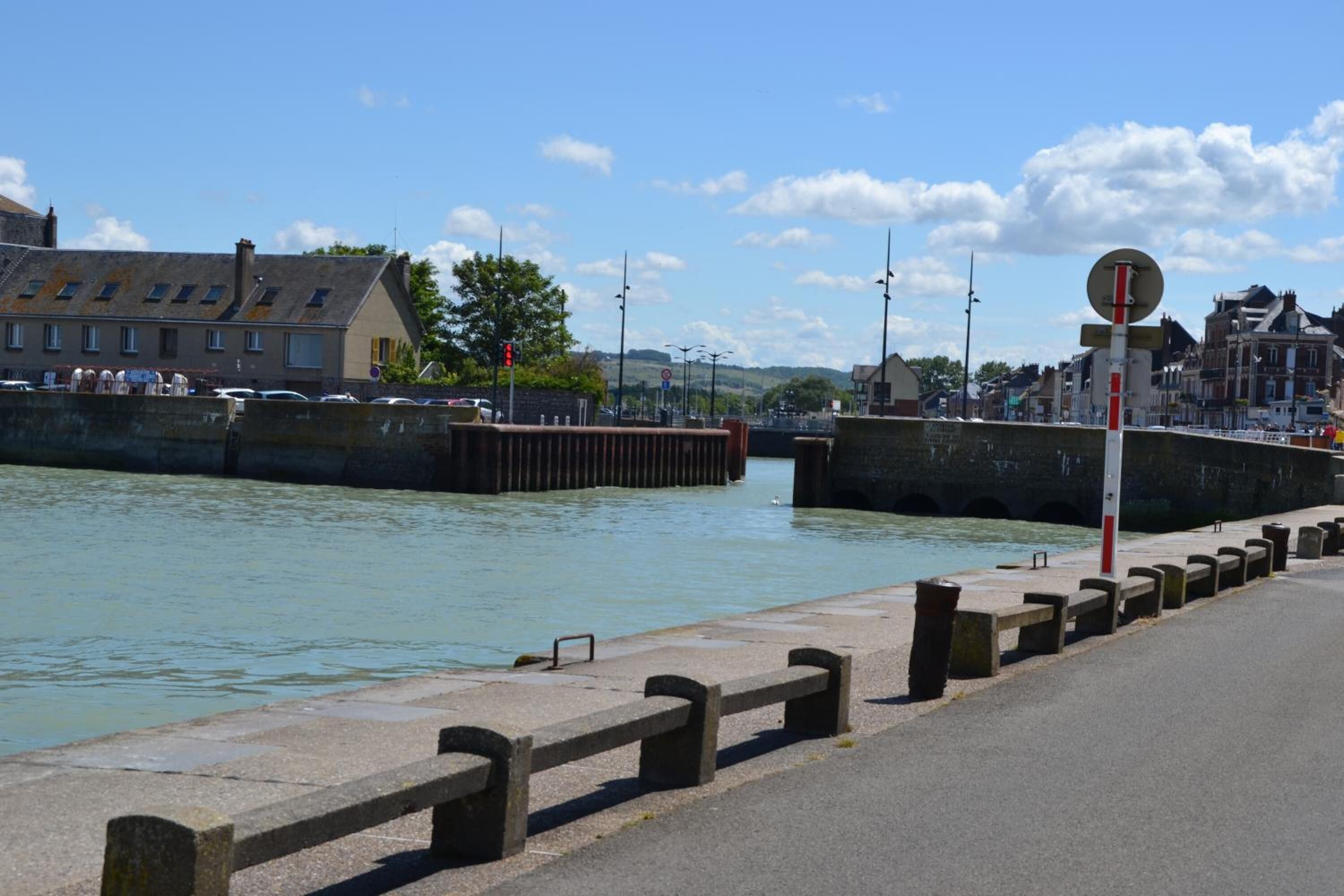 A waterfront promenade with a stone railing, a bridge, and buildings in the background.
