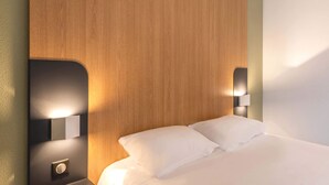 A hotel room with a wooden headboard, two bedside lamps, and a neatly made bed with white linens.