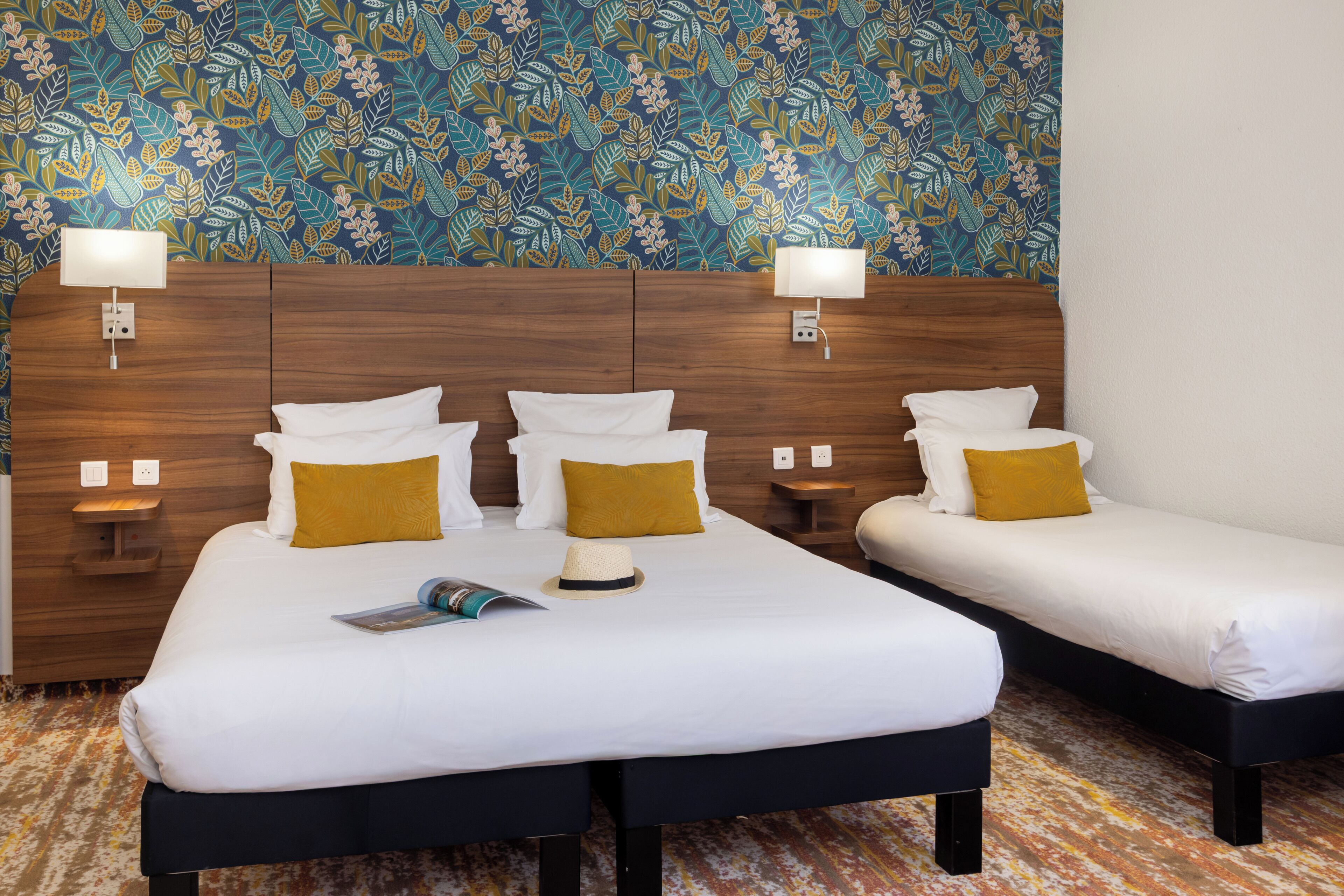 A hotel room with two beds, a wooden headboard, wall-mounted lamps, and a patterned wallpaper.