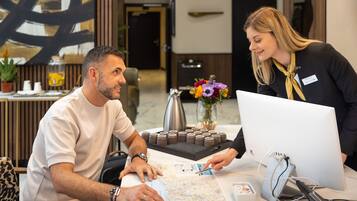 A man and a woman at a reception desk with a map, a computer, and a coffee pot.