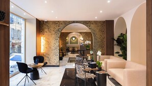 Eine moderne Lobby mit Marmorboden, schwarzen Sesseln mit Leopardenmuster, einem beigen Sofa und einem Empfangstresen.