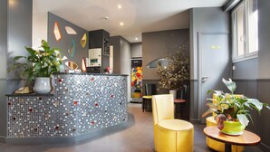 A reception area with a mosaic tile wall, a reception desk, and yellow seating. - Garden Saint Martin (Paris)