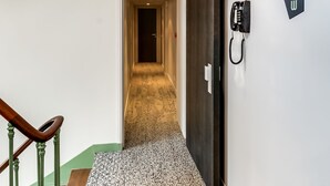 Een hotelgang met een tapijtvloer, een houten trap en een aan de muur bevestigd telefoontoestel.