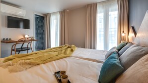 Een hotelkamer met een bed, een bureau met stoel, een aan de muur bevestigde televisie en een raam met gordijnen.