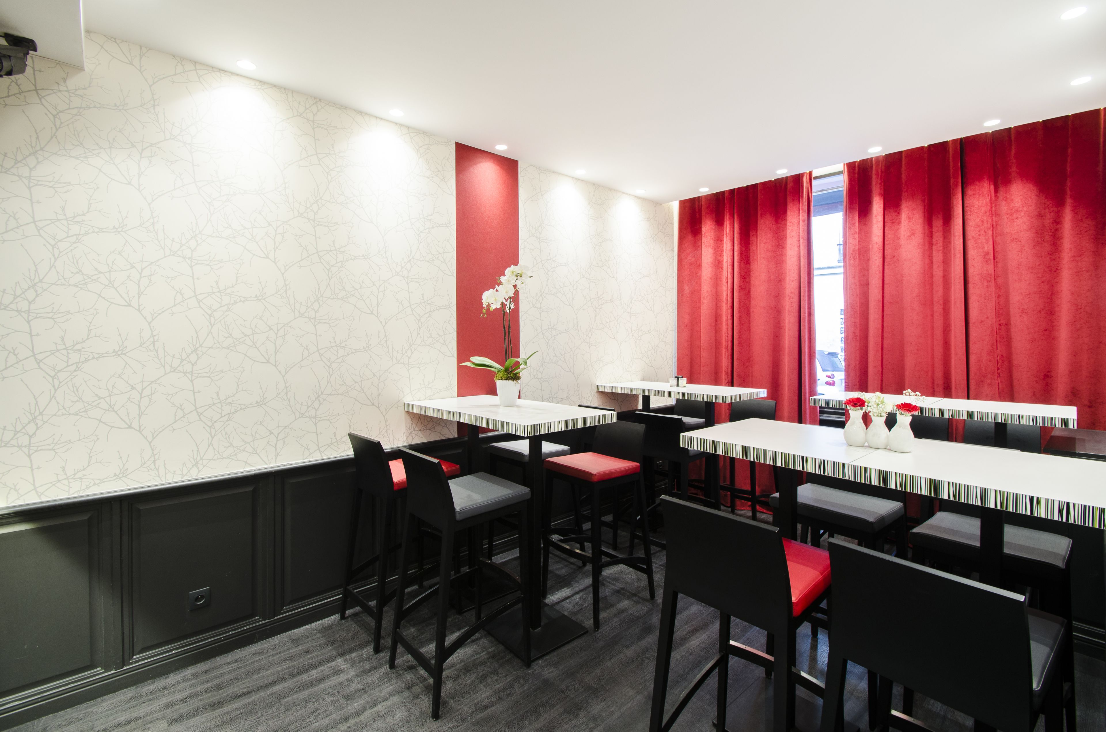 A restaurant with multiple tables and chairs, red curtains, and a potted plant on one table.