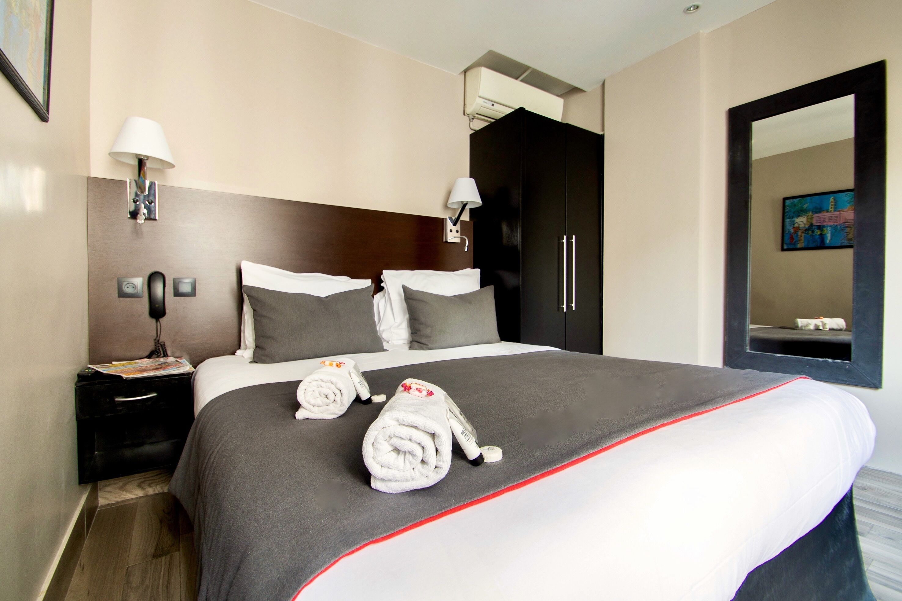 A hotel room with a large bed, two bedside tables, a wardrobe, a mirror, and a wall-mounted lamp.