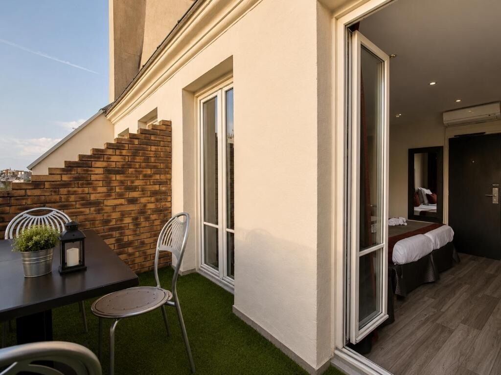 Ein Hotelzimmer mit einem Bett, einem kleinen Tisch mit Stühlen, einer Zimmerpflanze und einer Treppe, die zu einem Außenbereich mit Backsteinmauer und Kunstgrasanlage führt.