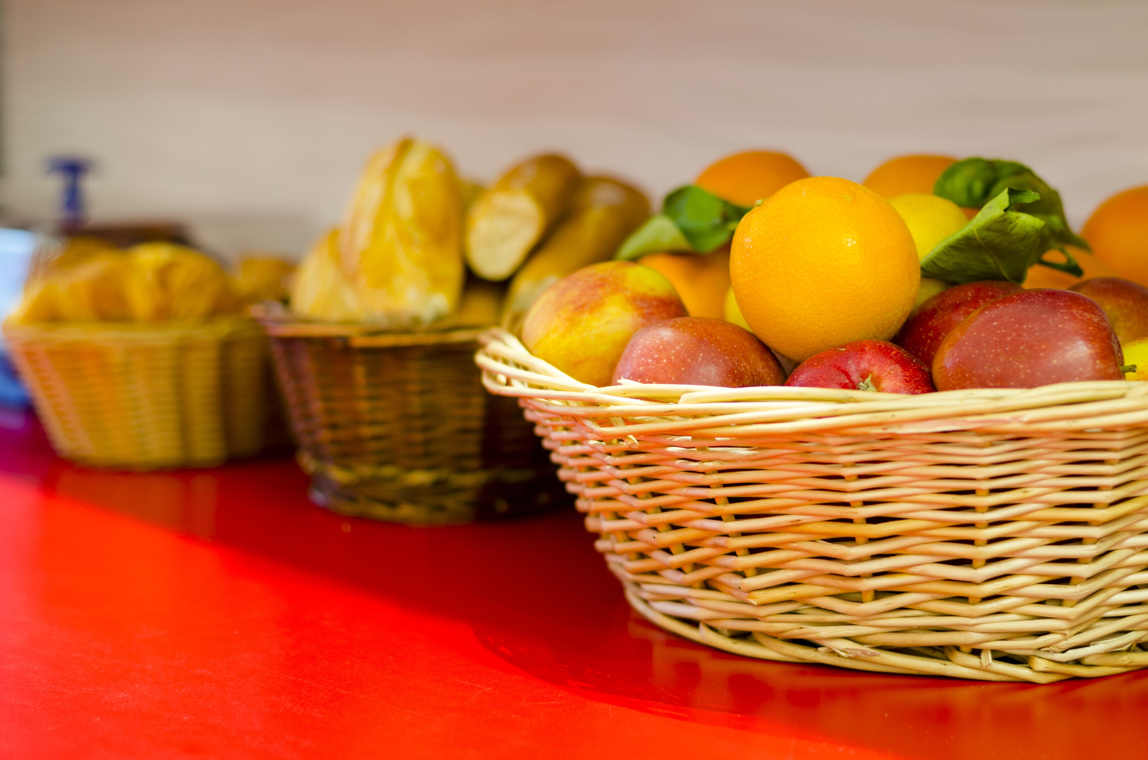 Three wicker baskets filled with fruits and bread on a red table.