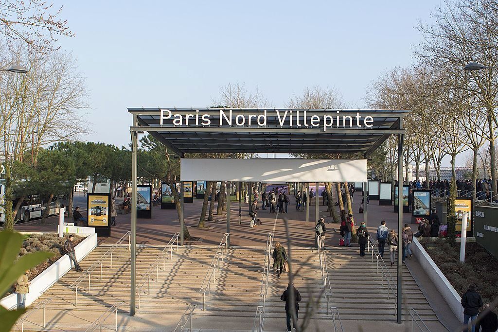 The entrance to Paris Nord Villepinte with a covered walkway and people walking.