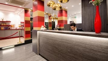 Eine Hotelrezeption mit modernem Design, inklusive einer Rezeptionstheke, einer roten Vase mit Blumen und einer Bar mit verschiedenen Accessoires.