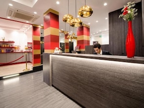 A hotel reception area with a modern design, featuring a reception desk, a red vase with flowers, and a bar area with various items. - Hotel Migny Opera Montmartre (Paris)