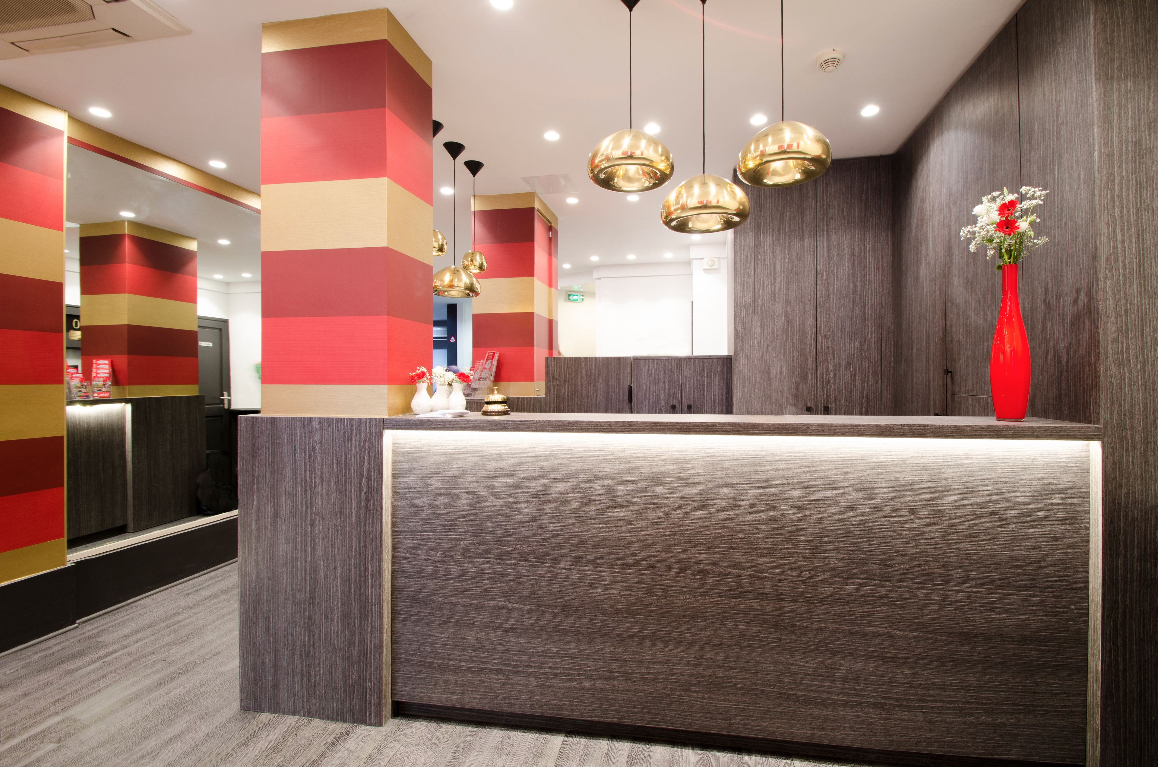 A modern reception area with a wooden reception desk, red and gold striped walls, and pendant lighting.
