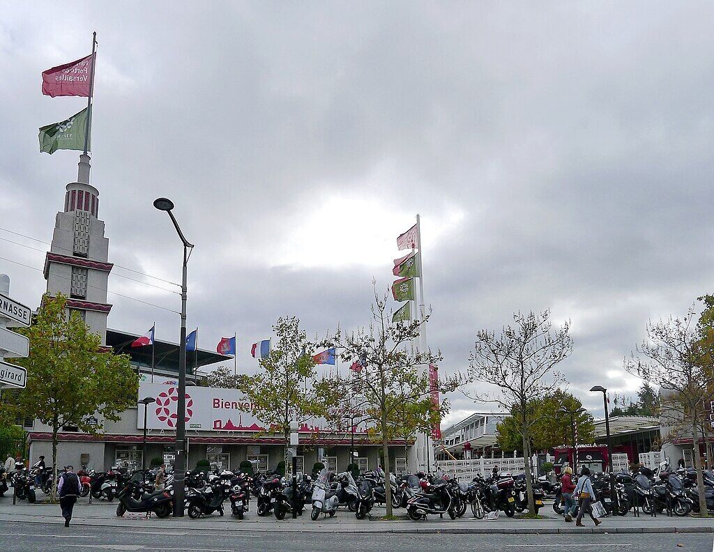 A busy street with multiple flags, a prominent building with a sign, and several parked motorcycles.