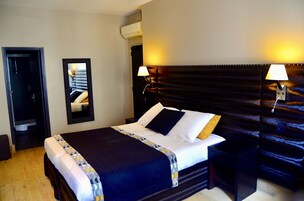 Una habitación de hotel con una cama grande, dos mesitas de noche, un espejo y una lámpara de pared.