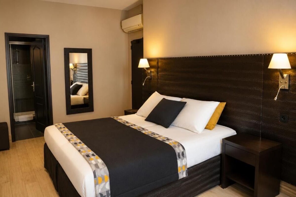 A hotel room with a large bed, bedside lamps, a mirror, and a wardrobe.