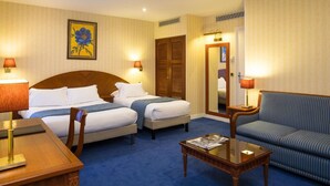 A hotel room with two beds, a sofa, a wooden coffee table, and a desk. - Hotel Impérial Paris (Paris)