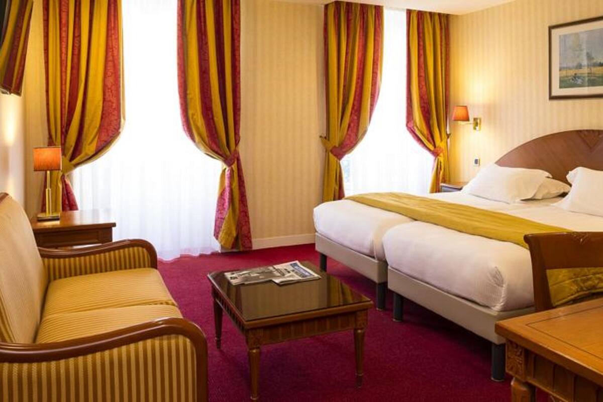 A hotel room with a bed, a desk, a chair, a table, and curtains.