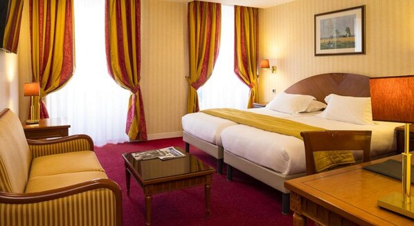A hotel room with a bed, a desk, a chair, a table, and curtains. - Hotel Impérial Paris (Paris)