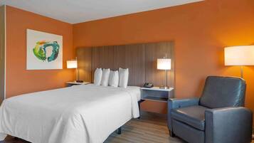 Ein Hotelzimmer mit einem großen Bett, zwei Nachttischen mit Lampen, einem grauen Sessel und einem Wandbild.