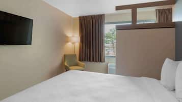 A hotel room with a large bed, a television mounted on the wall, a chair, and a window with curtains.