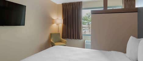 Habitación de hotel con una cama grande, televisión montada en la pared, una silla y una ventana con cortinas.