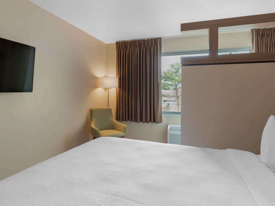 A hotel room with a large bed, a television mounted on the wall, a chair, and a window with curtains.