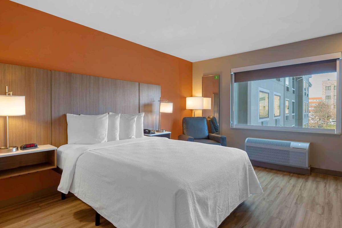 Une chambre d’hôtel avec un grand lit, deux tables de chevet, une chaise, une fenêtre donnant sur un beau paysage et un climatiseur fixé au mur.